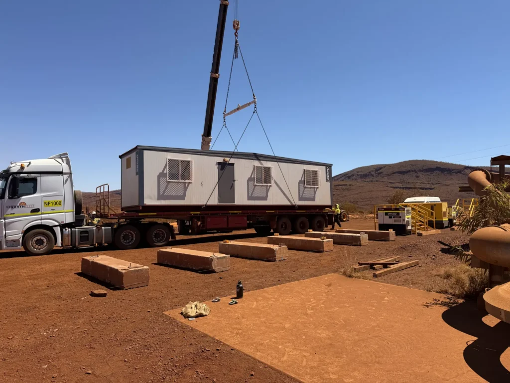 Crane lifting a donga onto a truck during site mobilisation in the Pilbara red dirt