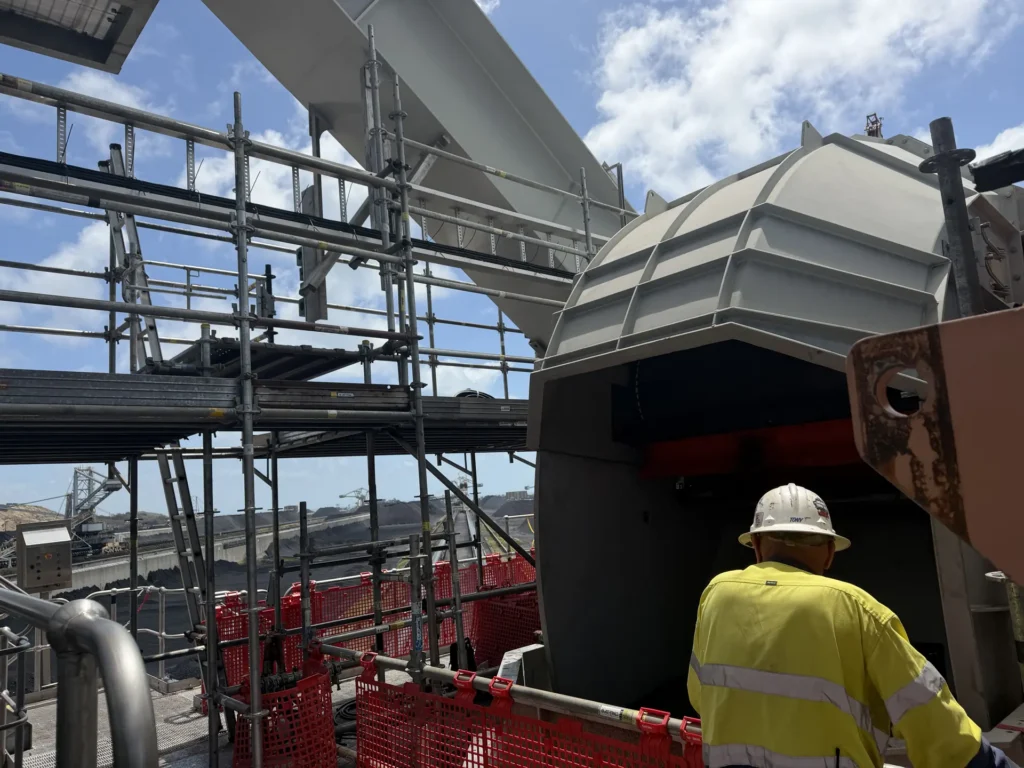 Tradesperson in a hard hat working on stacker equipment surrounded by scaffolding